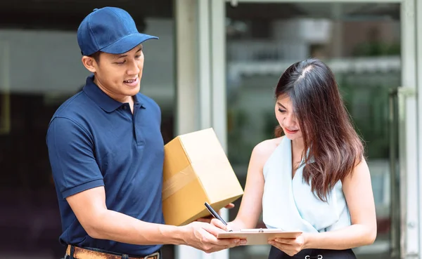 Asian delivery man holding a cardboard box while beautiful Asian woman putting signature in clipboard