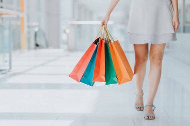 Alışveriş merkezinde yürürken renkli alışveriş çantaları taşırken genç kadın bacak görüntüsünü kapatmak