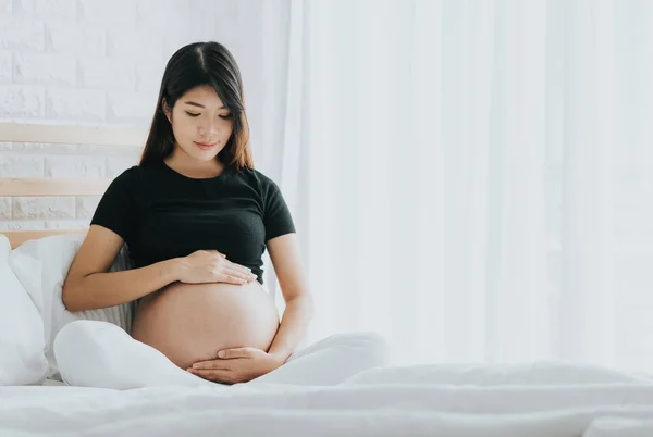 Mutlu Asyalı hamile kadın yatak odasında özenle beline dokunmadan. 