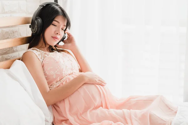 Mutlu Asya hamile kadın yatakta oturuyordu kulaklık müzik dinlemek