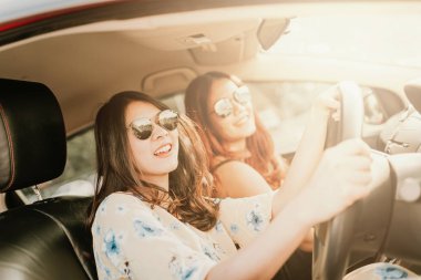 Gülüyor ve tatil bir yol gezisi sırasında arabaya gülümseyen genç mutlu Asyalı kız arkadaşlarım.
