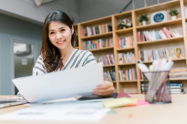 Dizüstü bilgisayar ve belge masada çalışma mutlu gülümseme iş veya öğrenci Asyalı kadın