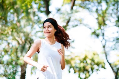 Parkta sabah güneş ışığı altında çalışan güzel mutlu sağlıklı Asyalı kadın