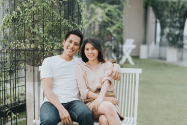 Mutlu Asya çift gülen ve having fun bemch açık otururken.