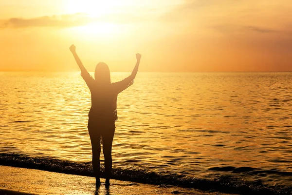 silhouette of happy woman celebrated success with arm up at the beach during sunset
