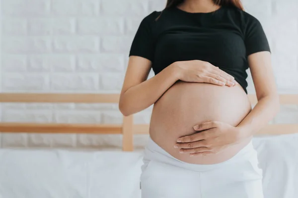 妊娠中の腹自宅ベッドの上の窓の近くに保持している妊娠中の女性の画像をトリミング — ストック写真