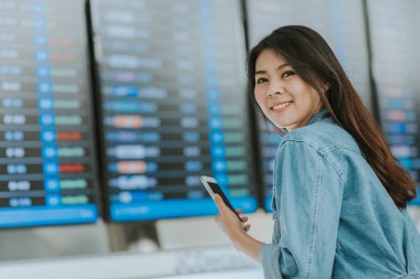 Havaalanı Uçuş bilgileri kurulu kamera arka plan bakmak ile Smartphone kullanarak mutlu Asyalı kadın