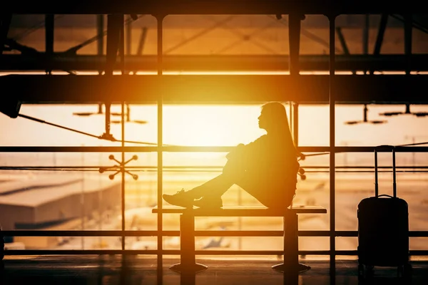Silhouette of woman passenger sitting in an airport lounge terminal with luggage waiting for flight aircraft