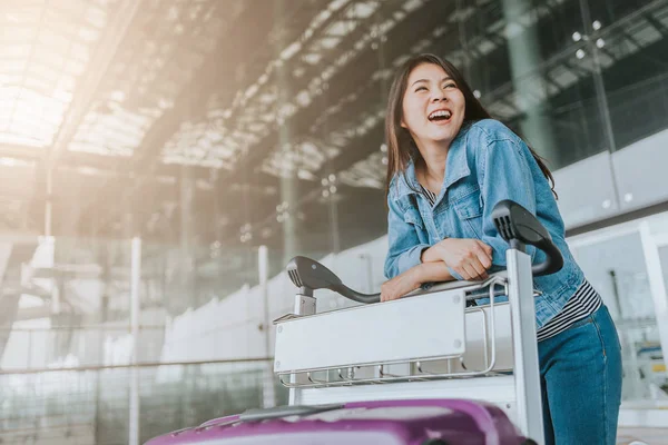 Mutlu genç çekici Asyalı kadın yolcu Bagaj arabası havaalanından geçirecekkimliği yürüyüş ile