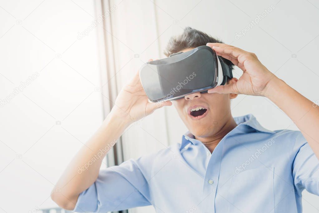 Asian man excited and surprised wearing virtual reality glasses case headset in living room. VR concept