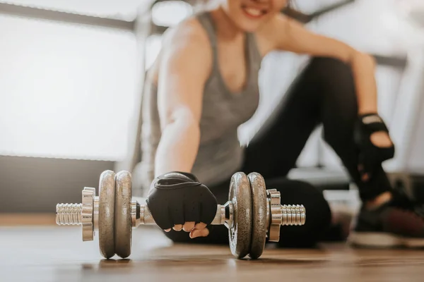 Happy woman picking up dumbbell on gym floor — Stock Photo, Image