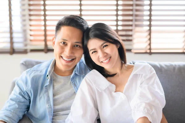 Asyalı çift evde kanepede dinlenirken gülümsüyor.