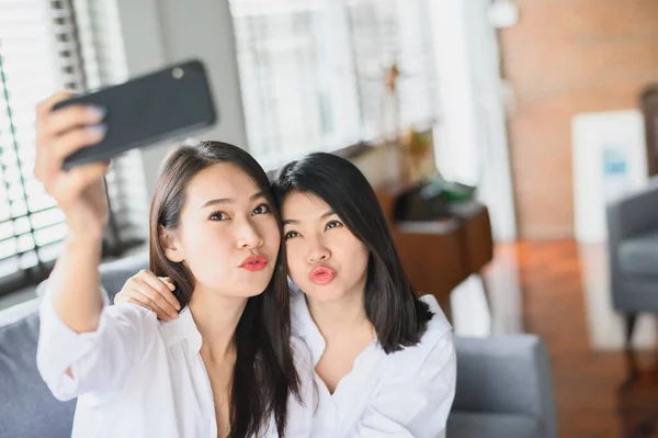 Счастливые азиатские подруги с помощью смартфона делают селфи в гостиной — стоковое фото