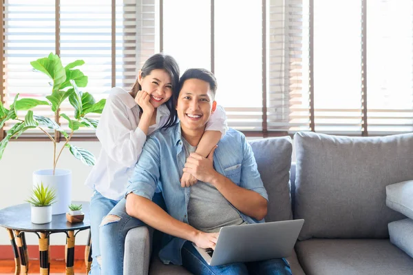 Glad asiatiska par i kärlek koppla av på soffan samtidigt som du använder laptop en — Stockfoto