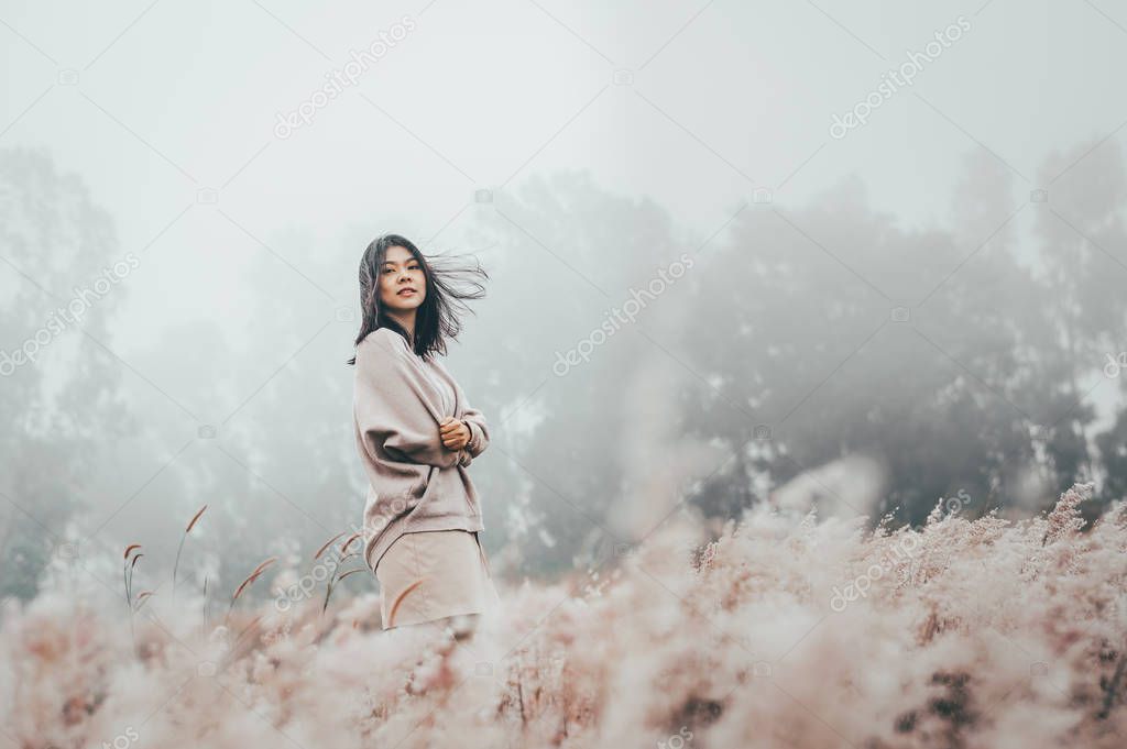 Asian woman standing in grass flower filed cover with mist 