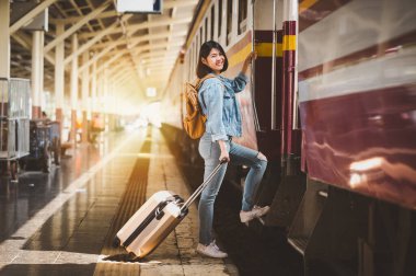 Gülümseyen Asyalı turist bavullarıyla tren istasyonunda trene biniyor. Etkin ve seyahat yaşam tarzı konsepti