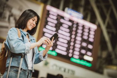 Mutlu gülümseyen Asyalı kadın gezgin akıllı telefon kullanarak tren istasyonu terminalinde yön bulmaya çalışıyor. 
