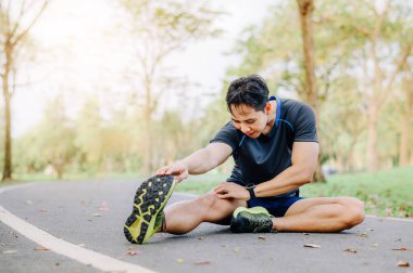 Sporcu genç Asyalı erkek, parkta koşuda bacağını esnetiyor.