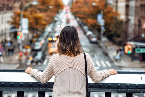 Beautiful woman travel and looking at New York City street with car traffic and yellow trees at autumn time from high point. View from the back. — Stock Photo, Image