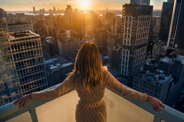 Rich woman enjoy the sunset standing on the balcony at luxury apartments in New York City. Luxury life concept.