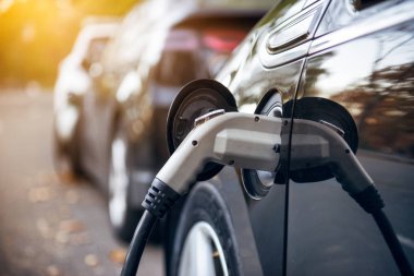 Elektrikli araba, şehir caddesinde elektrikli araba şarj istasyonuyla park yerinde şarj oluyor. Elektrikli arabalar hazır bekliyor.