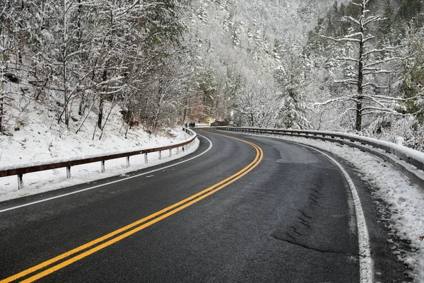 Красивый зимний пейзаж с шоссе с поворотом и заснеженными деревьями. Чистый горный асфальт зимняя дорога с желтой маркировкой двойные линии и знак — стоковое фото