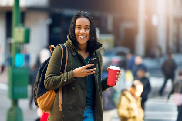 Frumoasă studentă latină care bea cafea în aer liber pe strada orașului și trimite mesaje text pe telefonul mobil. Frumos tanara studenta fata cu o geanta zâmbind în aer liber . — Fotografie, imagine de stoc