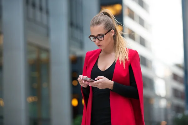 O femeie de afaceri care utilizează aplicația mobilă pe telefonul mobil și se plimbă de la clădirea de birouri din New York City — Fotografie, imagine de stoc
