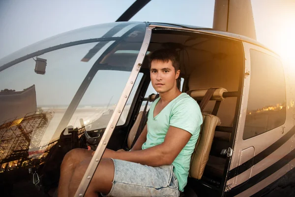 Joven hombre guapo sentado en la cabina del helicóptero. Piloto de helicóptero privado listo para volar en la ciudad en un día soleado brillante . —  Fotos de Stock