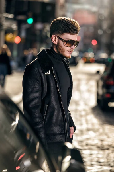 Handsome bearded man in leather jacket and sunglasses walking on city street — Stock Photo, Image