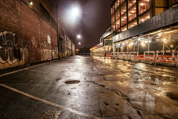 Estrada de rua asfalto na cidade da noite após a chuva. Estacionamento com graffiti nas paredes de tijolo . — Fotografia de Stock