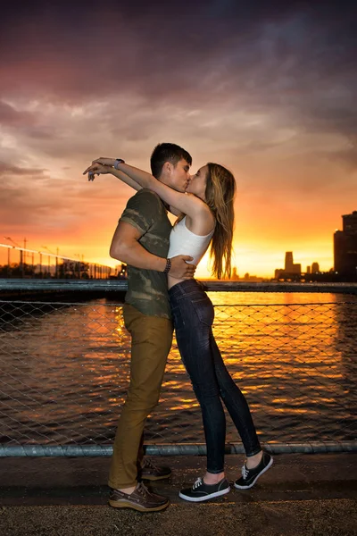 Young beautiful couple in love kissing near the ocean pier in city at sunset time — Stock Photo, Image
