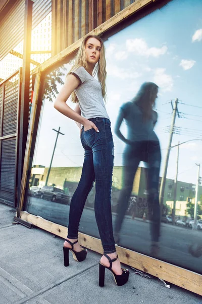 Güzel genç kız mavi kot pantolon ve siyah yüksek topuklu giyen ve açık havada şehrin sokak poz uzun bacaklar ile — Stok fotoğraf