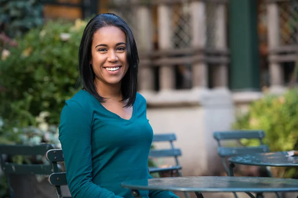Vacker ung afroamerikansk flicka sittande på gatan café och leende tittar på kameran — Stockfoto