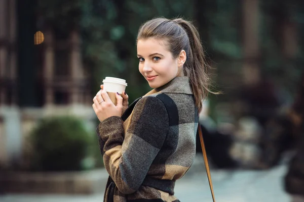 Hermosa mujer de negocios sosteniendo la taza de café y caminando por la calle de la ciudad al trabajo en primavera. Estilo de vida brote de mujer adulta linda . —  Fotos de Stock