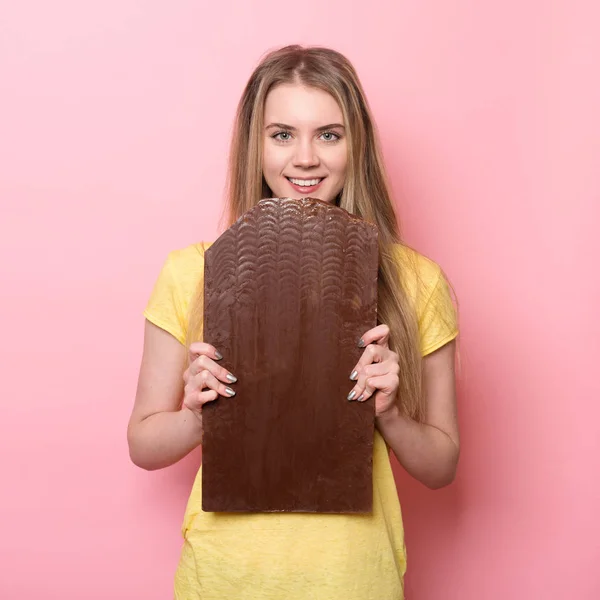 Vrouw met chocolade glimlachen. Leuk meisje te houden en het eten van gigantische cacao chocolade bar in de buurt van roze muur — Stockfoto