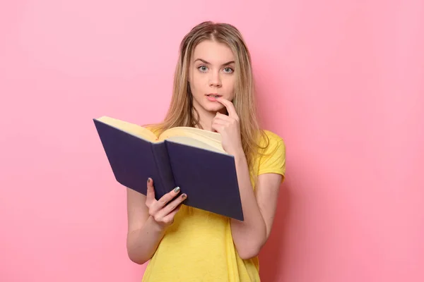 Förvirrad söt flicka tänkande och läser boken isolerad på färgglada rosa bakgrund — Stockfoto