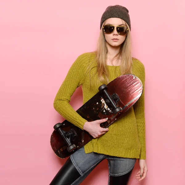 Menina elegante hipster segurando skate e posando perto da parede rosa vestindo roupas de rua casual estilo elegante . — Fotografia de Stock