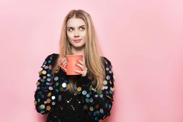 Linda chica feliz mantenga taza de café y mirando hacia un lado y soñando. Mujer bebiendo café cerca de la pared rosa . —  Fotos de Stock