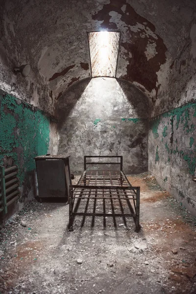 Abandoned prison cell room with old rusty bed frame and peeling walls. Philadelphia Eastern State Penitentiary