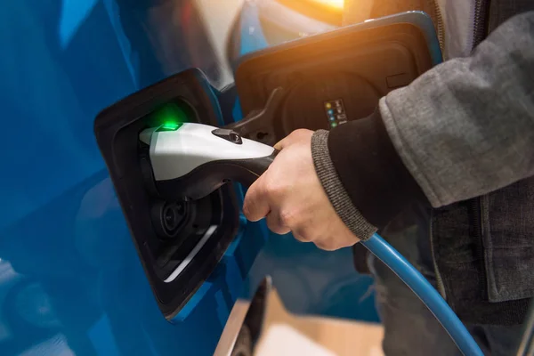 Man charging electro car at charging station. Man holding in hand power cable supply plugged in charging port