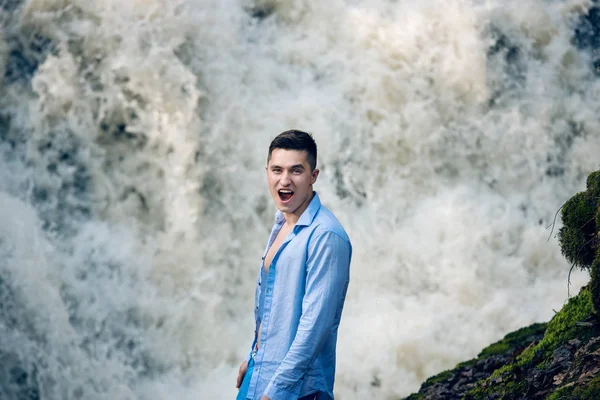 Exited šťastný muž, stojící poblíž vodopád a při pohledu na fotoaparát. Lidé cestují životní styl na téma přírody dobrodružství. — Stock fotografie