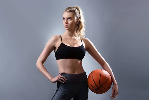 Hermosa mujer jugador de baloncesto de pie y sosteniendo pelota de baloncesto — Foto de Stock