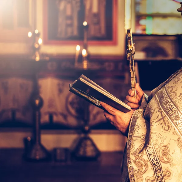 Священник молится в церкви, держа в руках святую Библию и крест — стоковое фото