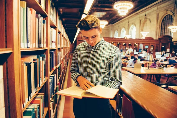 Człowiek w czytelni biblioteki wziął książkę z półki i czytanie — Zdjęcie stockowe