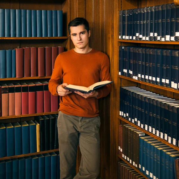 Homem com um livro em pé nas prateleiras da biblioteca vintage — Fotografia de Stock