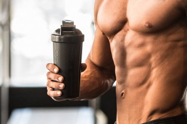 Kusursuz bir beden ile adam protein shaker spor salonunda egzersiz yaptıktan sonra tutar.