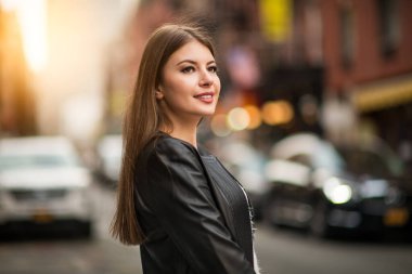 Hoş bir gülümsemesi olan güzel bir kadın. Deri ceket giymiş ve yan tarafa bakıyor.