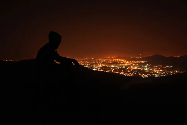 Gece şehir manzaralı gözlemleyerek tepenin üstünde genç adam.