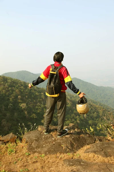 Jovem com mochila e capacete em pé no topo de uma montanha e desfrutando de vista para o vale — Fotografia de Stock